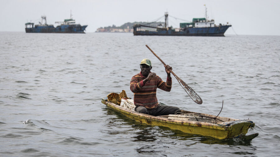 A fisherman paddles in front of commercial fishing boats off the coast of Dakar, Senegal. Credit: John Wessels/AFP via Getty Images