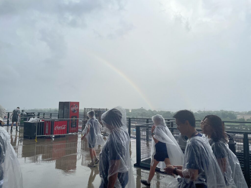 People in see-through raingear walk in the foreground, with the rainbow in the background