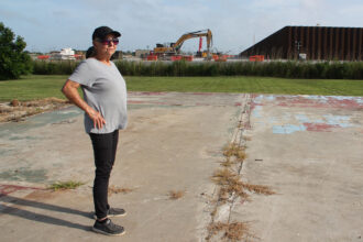 Sherry Peshoff stands on a slab where a home use to sit next to the perimeter wall of Venture Global’s CP2 terminal in Cameron, La. Credit: Nicholas Kusnetz/Inside Climate News