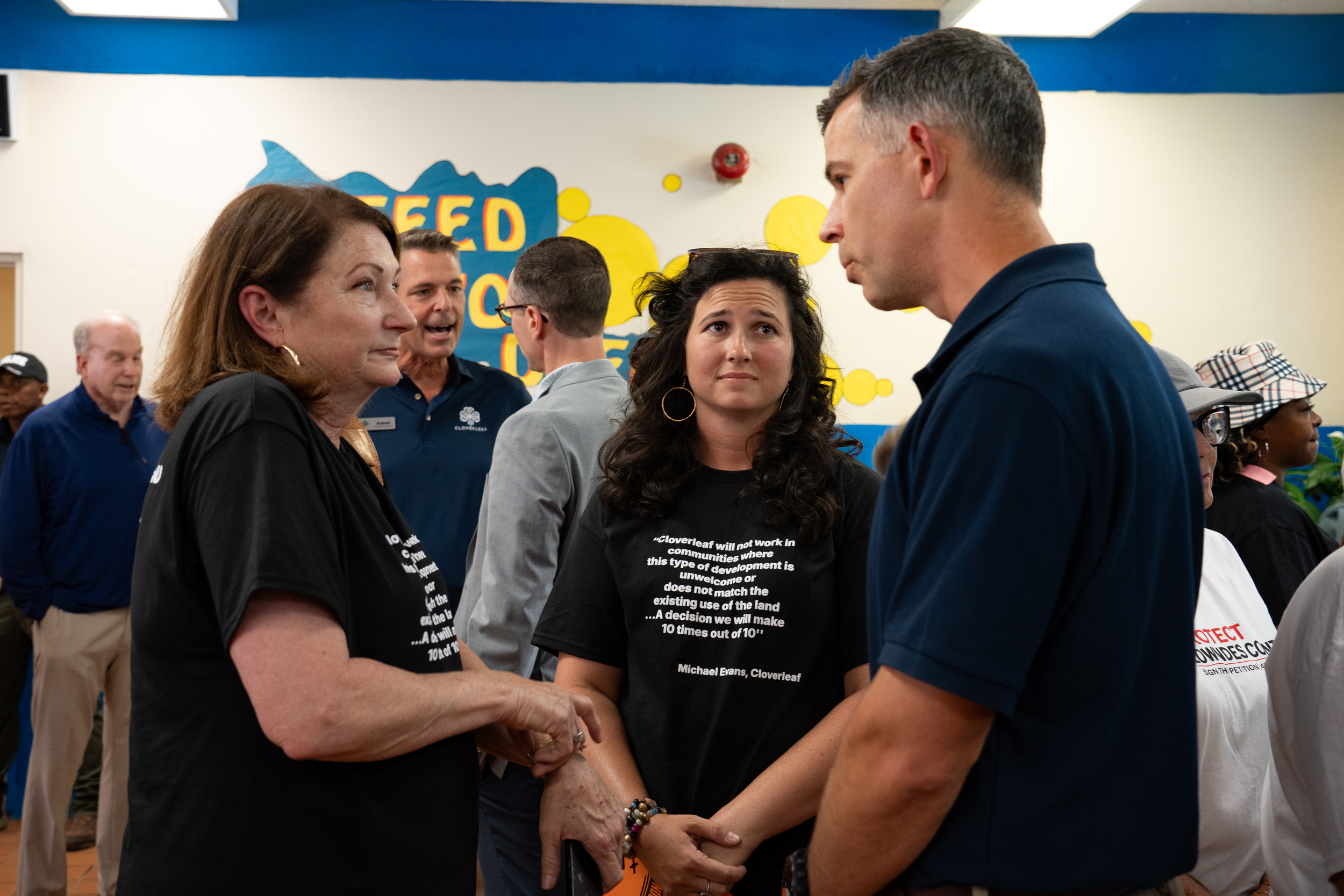 Ann Burgwin Faulkner (center) and her mother speak with Michael Evans of Cloverleaf, whose quote is on their shirts. Credit: Lee Hedgepeth/Inside Climate News