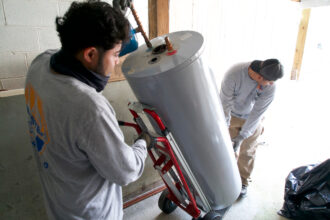 Technicians remove a natural gas water heater from a home to be replaced with an electric heat pump. Credit: Bastien Inzaurralde/AFP via Getty Images