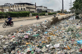 People ride past a drain clogged with plastic waste along a roadside in Karachi, Pakistan, on Aug. 24, 2025. Credit: Asif Hassan/AFP via Getty Images