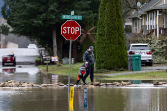 A father helps his son walk over a path made of sandbags following severe flooding on Dec. 12, 2025, in Burlington, Wash. Credit: Natalie Behring/Getty Images