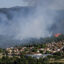Thick smoke rises from a mountain range overlooking the community of Vinca, France, tucked between trees.