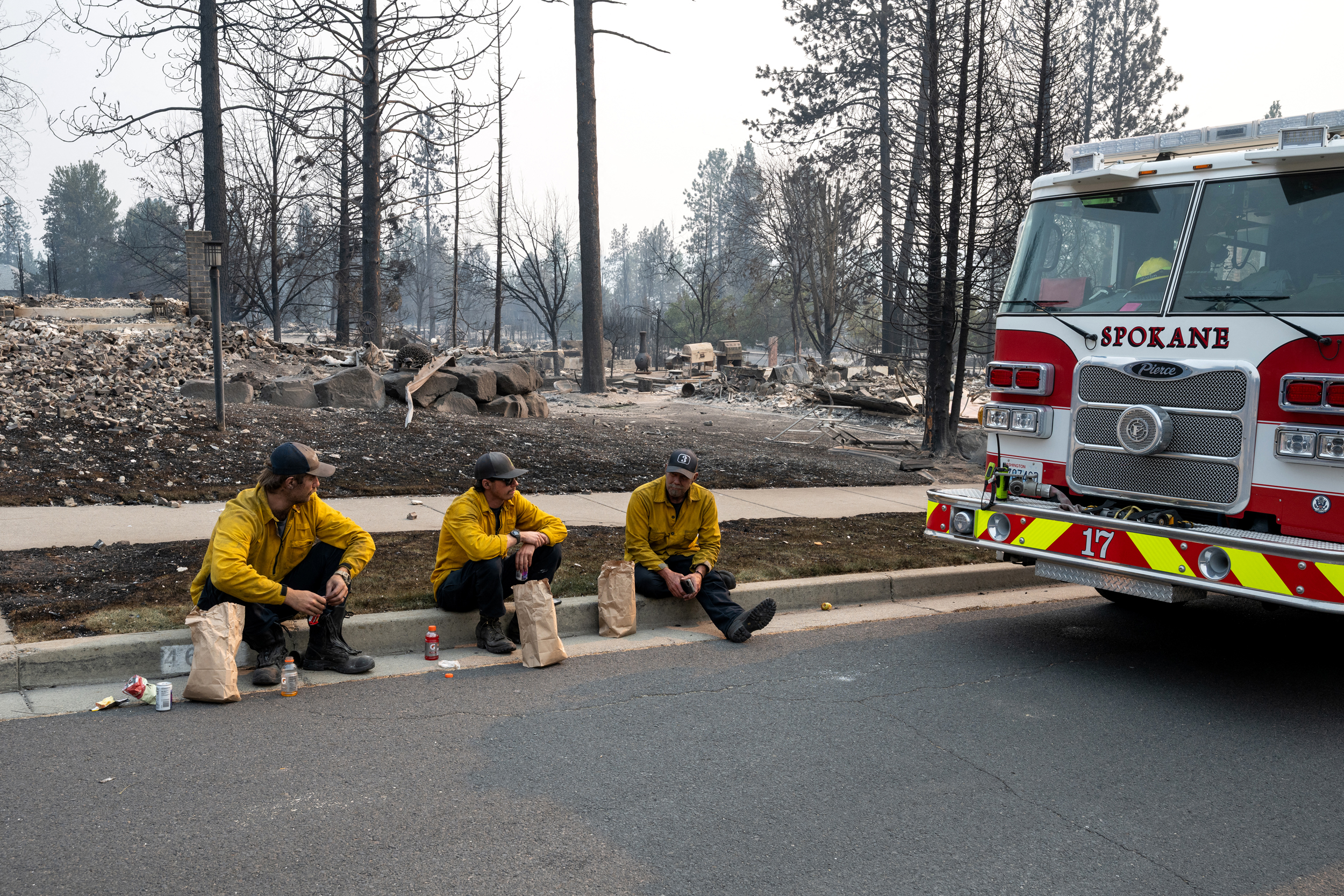 Members of the Spokane Fire Department sit on a curb in front of burned residential homes in the Balboa neighborhood of Spokane on Aug. 2. Credit: Erick Doxey/AFP via Getty Images