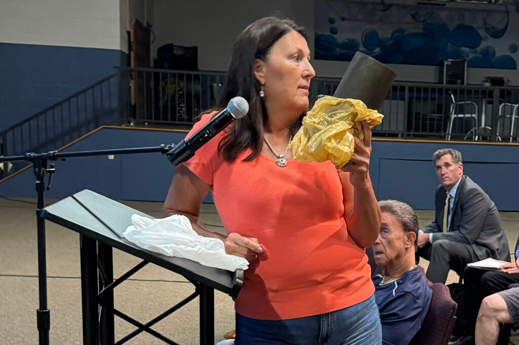 Mount Eyre Manor resident Kim Brunnquell shows a blackened filter from her home water treatment system at a community meeting in July over the Energy Transfer pipeline leak that has upended their neighborhood. Three months earlier, the filter had been white. Credit: Marianne Lavelle/Inside Climate News