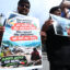 Several people are visible in the photo holding signs. One reads: "You emitted the carbon: we suffered the destruction. You caused the emissions: We lost our lives."