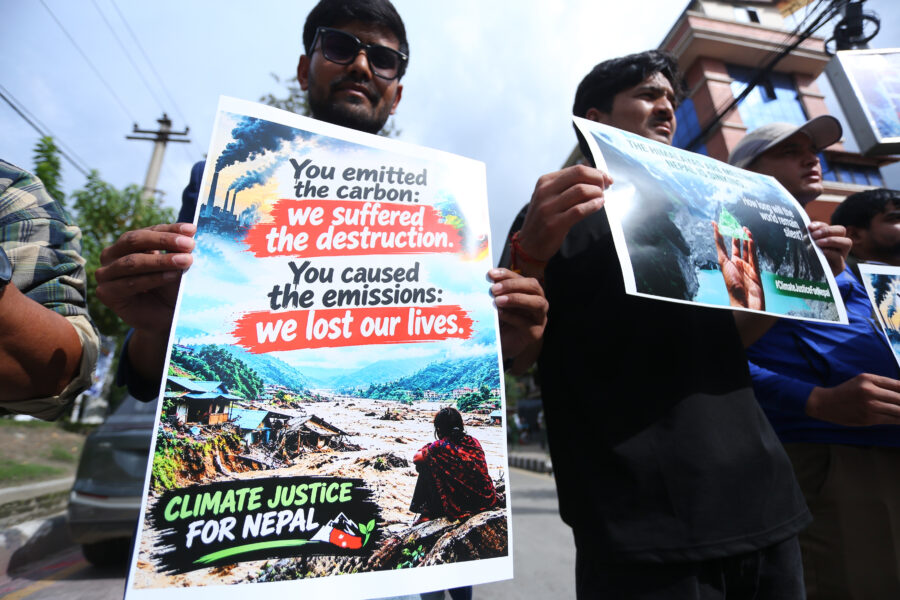 Several people are visible in the photo holding signs. One reads: "You emitted the carbon: we suffered the destruction. You caused the emissions: We lost our lives."