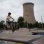 A child plays on a scooter in the park, with the cooling tower looming in the background.