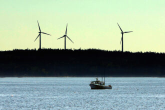 Wind turbines stand in the background as a lobster boat moves through the waters off Vinalhaven, Maine. Credit: Gregory Rec/Portland Press Herald via Getty Images