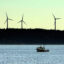 Wind turbines stand in the background as a lobster boat moves through the waters off Vinalhaven, Maine. Credit: Gregory Rec/Portland Press Herald via Getty Images