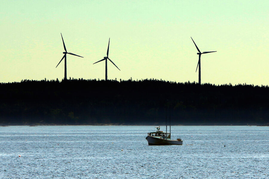 Wind turbines stand in the background as a lobster boat moves through the waters off Vinalhaven, Maine. Credit: Gregory Rec/Portland Press Herald via Getty Images