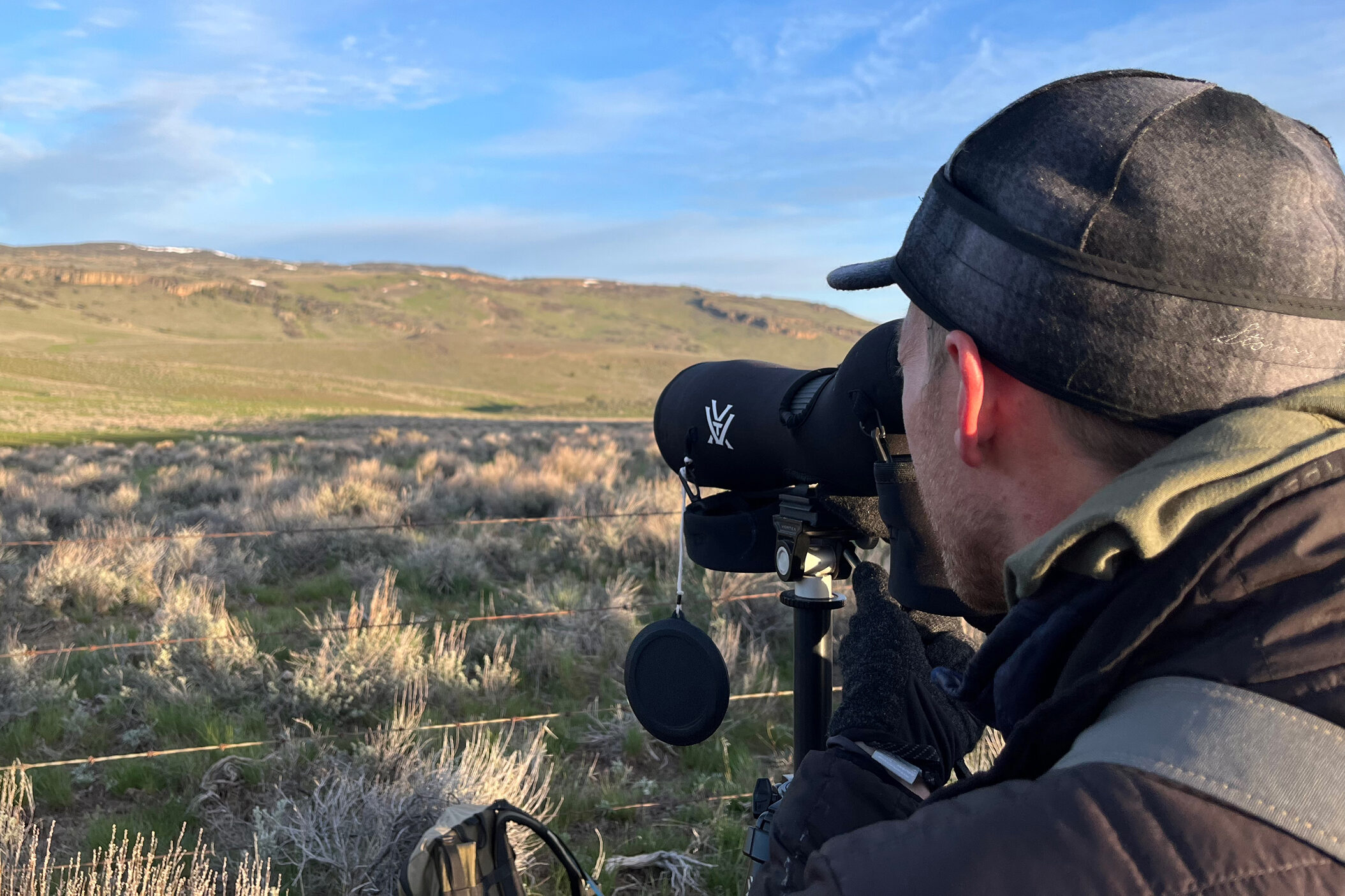 Skyler Vold spots sage grouse through his spotting scope as they conduct their mating dances at a lek in Oregon on April 23, 2024. Credit: Wyatt Myskow/Inside Climate News