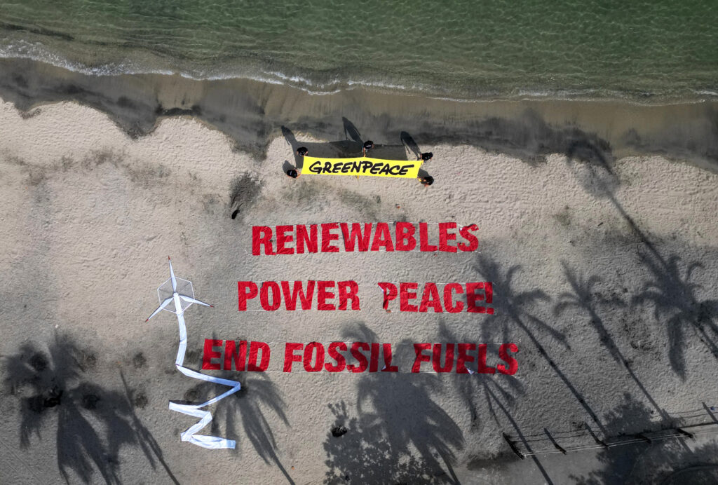 Aerial view of members of Greenpeace next to a sign reading "Renewables Power Peace! End Fossil Fuels" during the First
