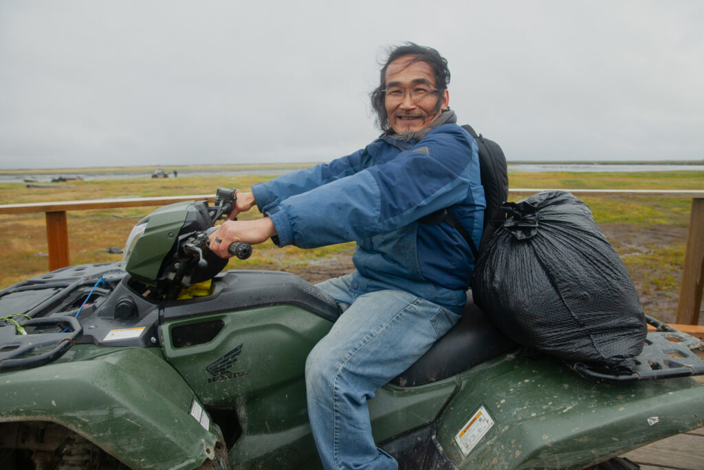 Wassilie Andrew, the maintenance worker at the Kwigillingok school, rides his four-wheeler on a boardwalk. A lifelong village resident, he remembers when Kwigillingok had hills, and the tundra was frozen. Credit: Olga Loginova/Inside Climate News 