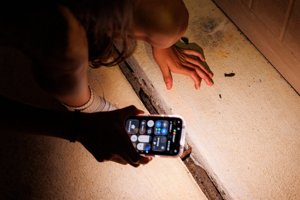 Aaliyah Pacheco uses her cellphone flashlight to examine deep cracks exposing rebar in the driveway of her family’s home. Credit: Sam Owens/San Antonio Express-News