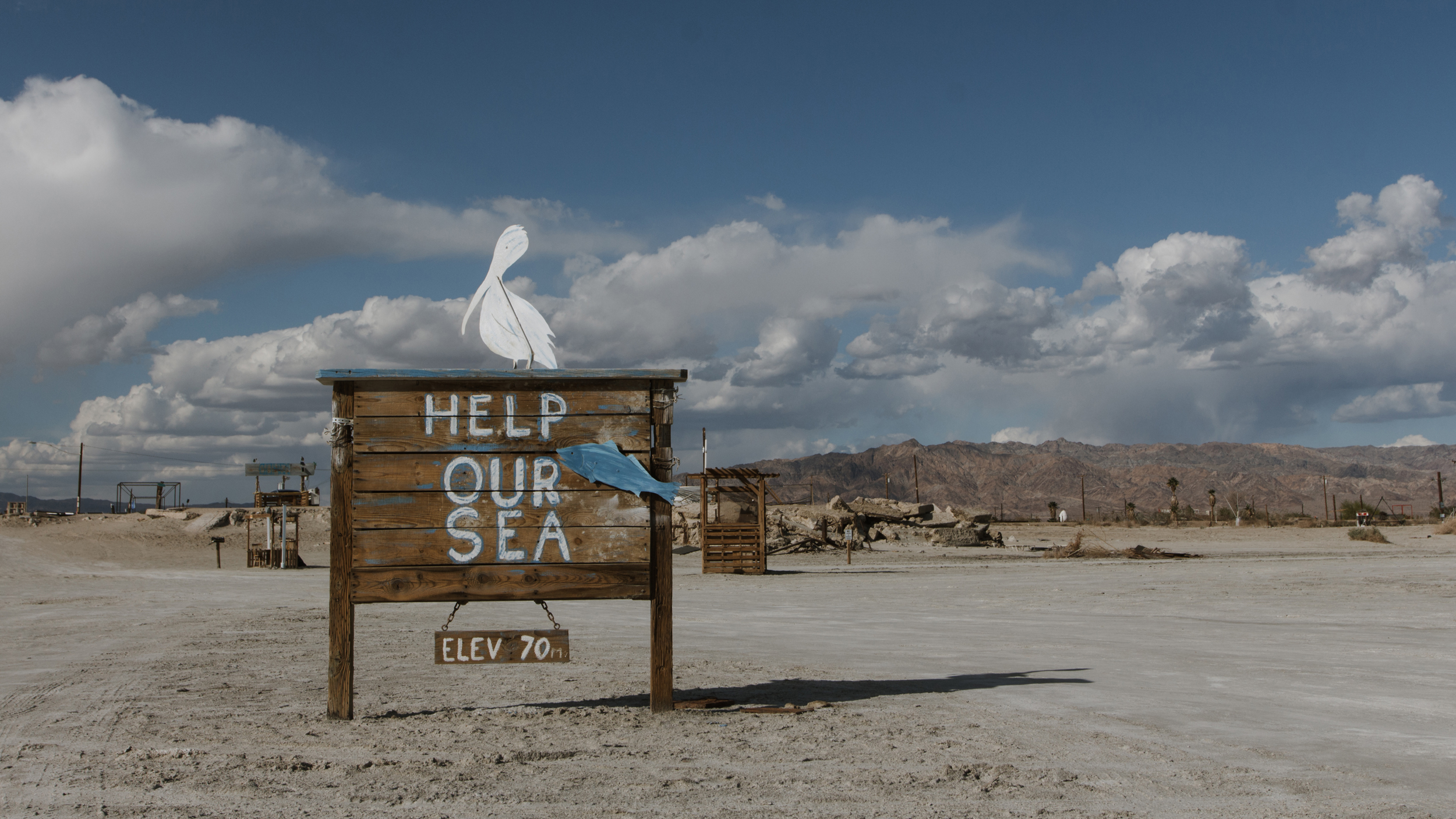 Another art installation in Bombay Beach calls to “Help Our Sea,” invoking the Salton Sea’s ecological decline. As the lake shrinks and grows more saline, it has become increasingly inhospitable to fish and threatens important habitat for birds that depend on the sea along the Pacific Flyway. Credit: Carla Samon Ros/CJI
